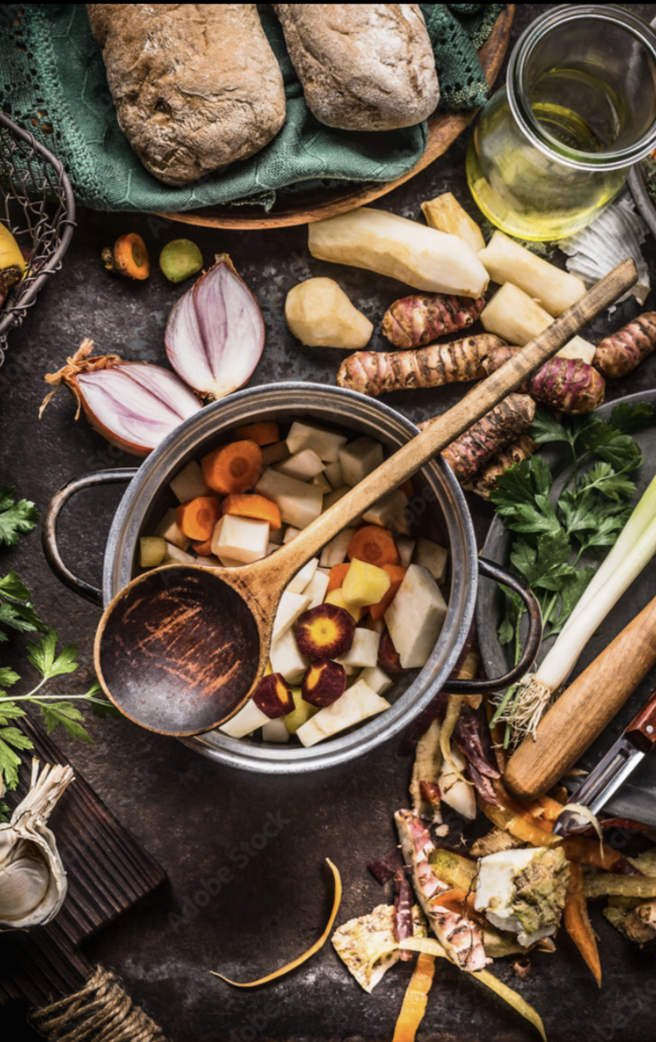 Overhead view of a pot of chopped carrots, parsnips and Jerusalem artichokes with a wooden spoon, bread and olive oil
